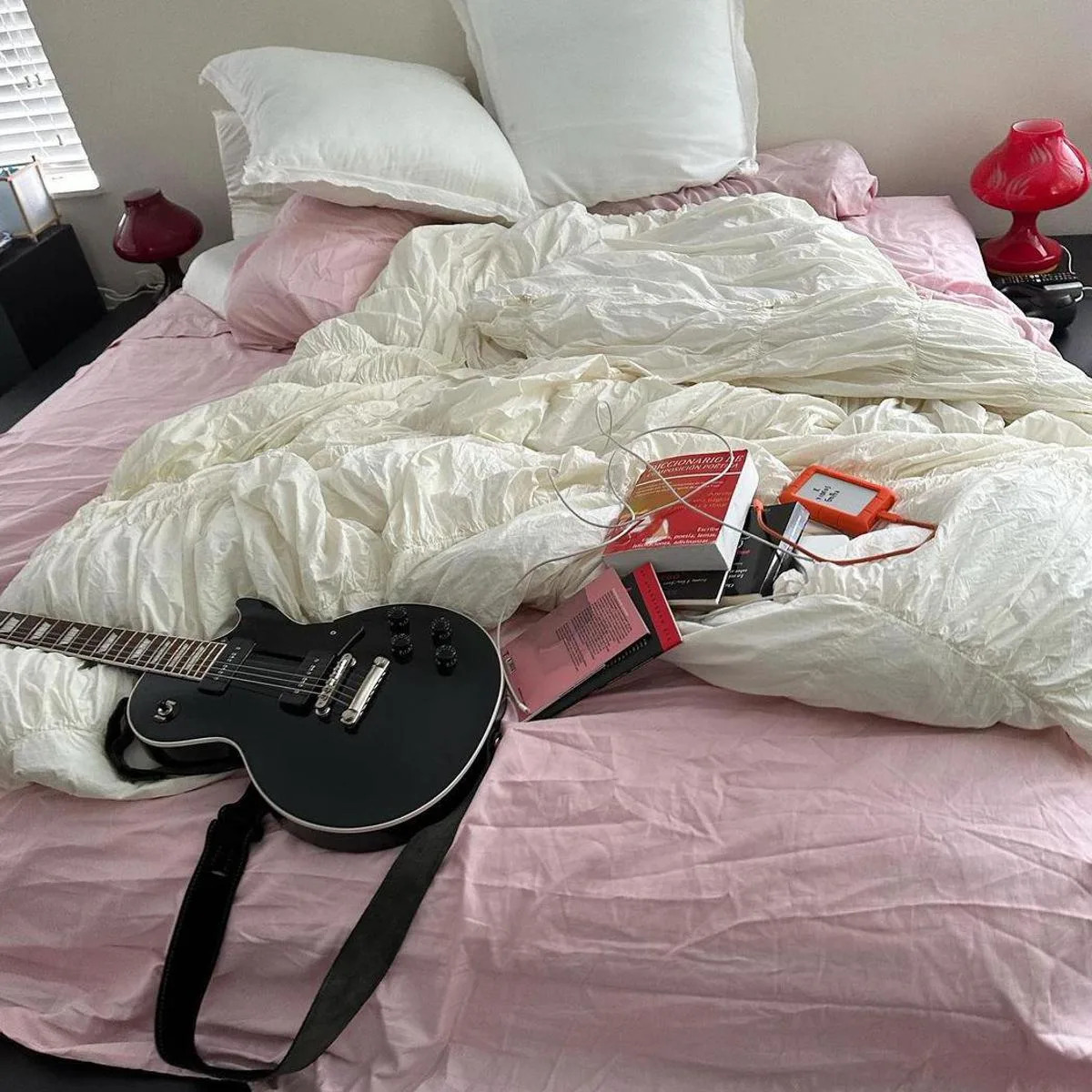 Cama de dos plazas sin hacer con libros y una guitarra encima
