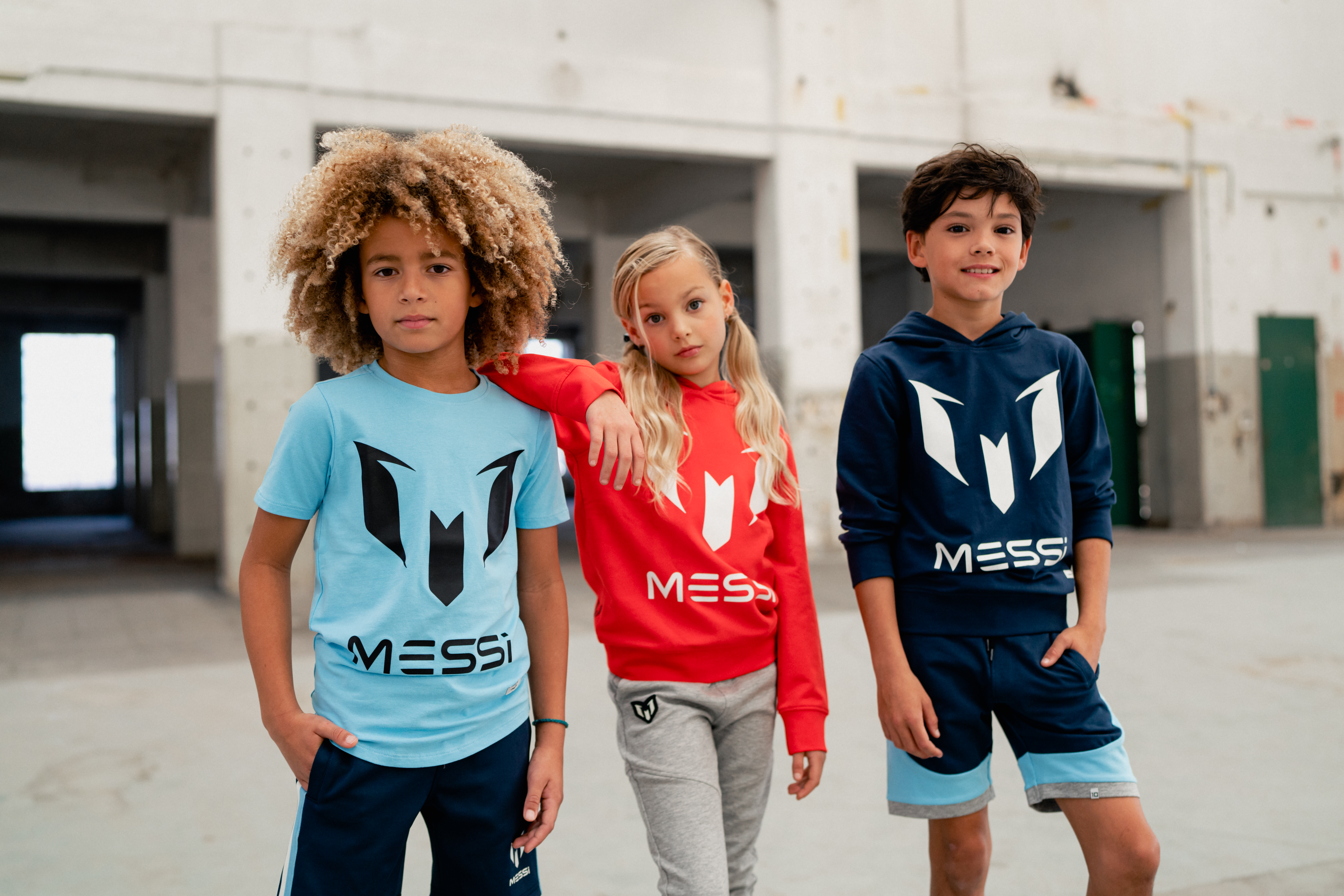 Dos niños y una niña posando con conjuntos deportivos de la marca